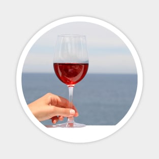 Hand with glass of wine, blue sea in background Magnet